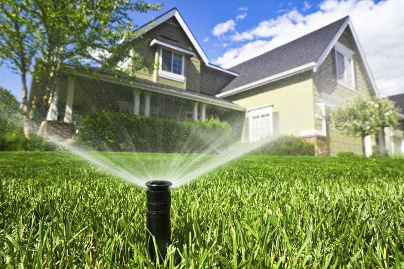 Sprinkler watering a green lawn in front of a house